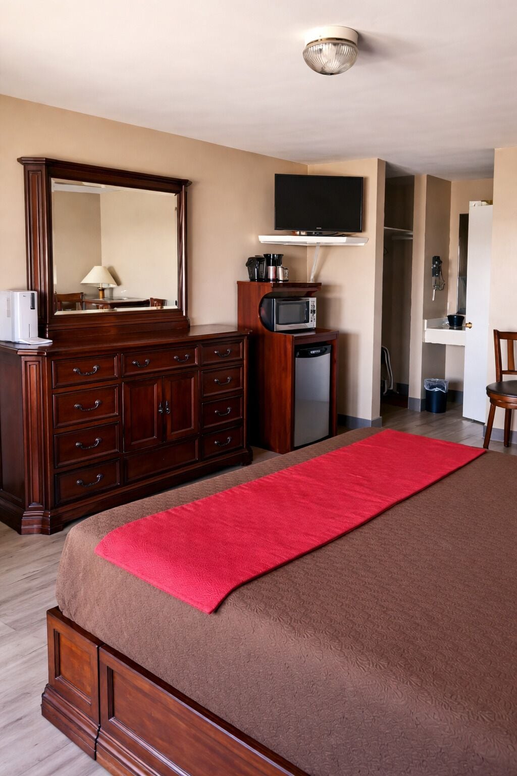 A hotel room with a large bed, a wooden dresser, a microwave, a television, and a red throw blanket.