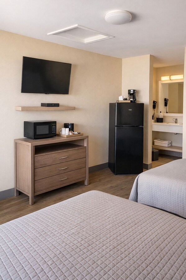 A hotel room with a bed, a desk with a microwave, a refrigerator, a TV, and a bathroom with a mirror and sink. - Venice Inn (Venice)