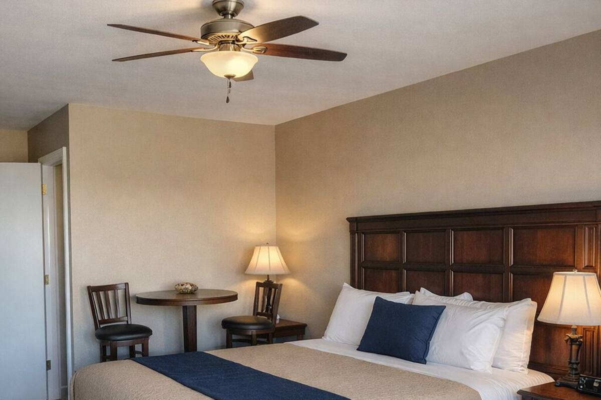 A hotel room with a large bed, a ceiling fan, a desk with a chair, and two bedside lamps.