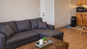 Ein Wohnzimmer mit einer Eckcouch, einer Holzkommode und einem kleinen Tisch mit Kerze und Pflanze.