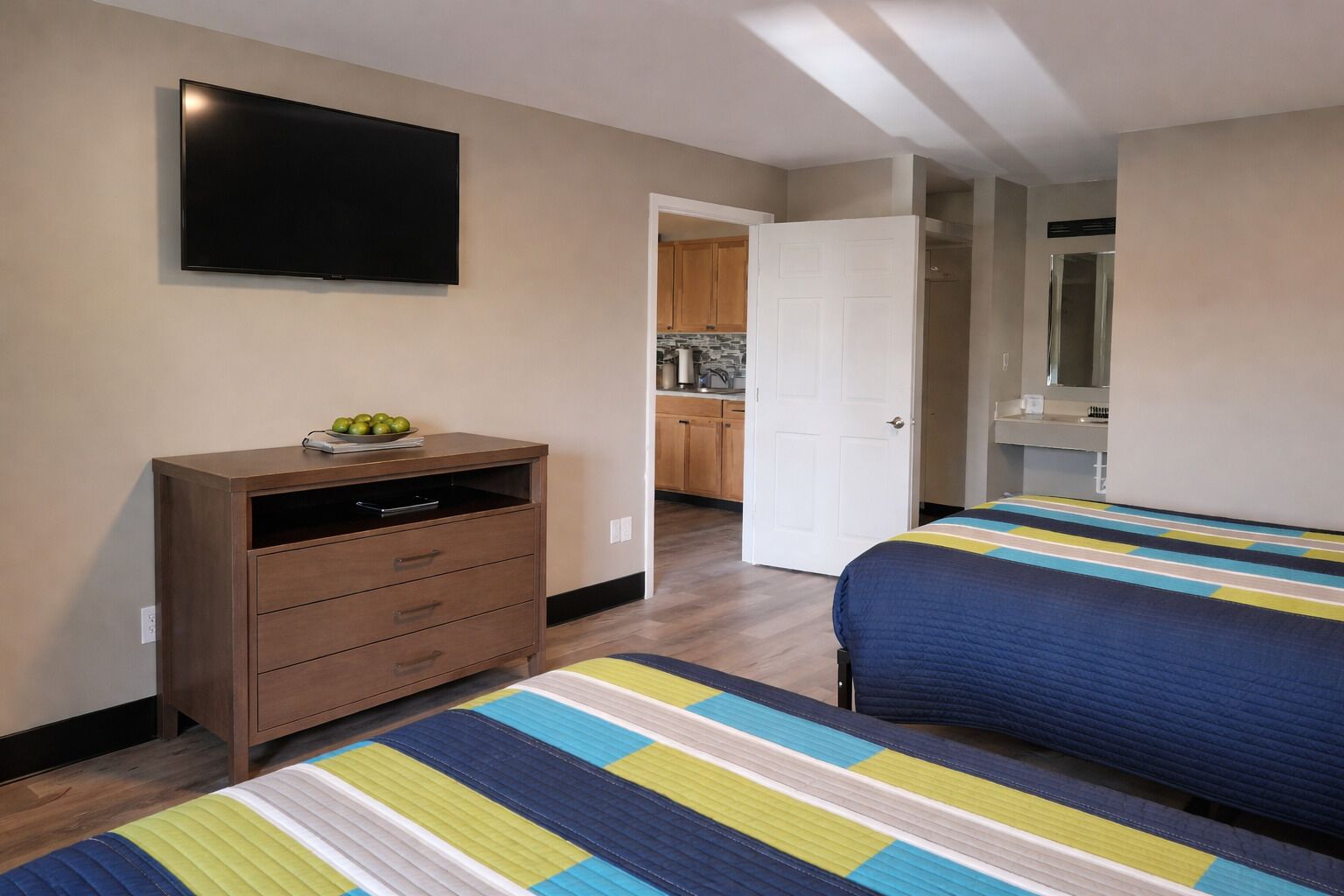 Une chambre avec deux lits, une commode, une télévision et une vue sur la cuisine.