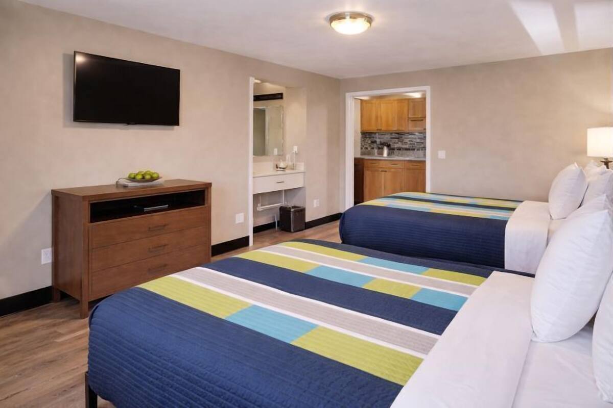 A hotel room with two beds, a TV, a dresser, a mirror, and a kitchenette.