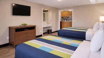 Une chambre d’hôtel avec deux lits, une télévision, une commode, un miroir et une kitchenette.
