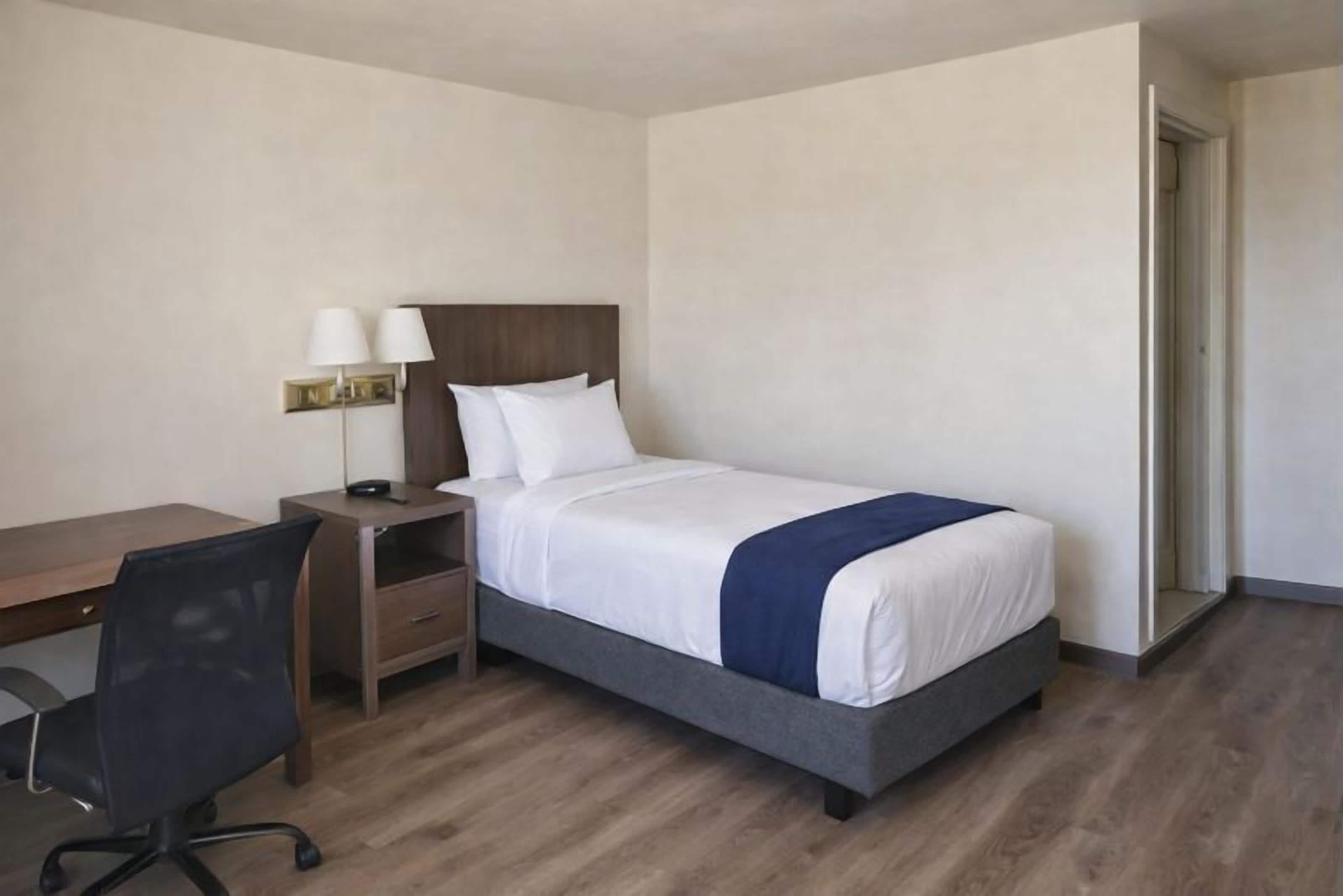 A hotel room with a bed, a desk, a chair, and a nightstand.