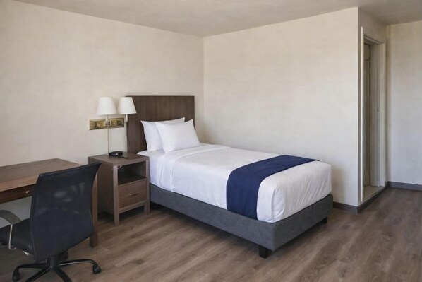Une chambre d’hôtel avec un lit, un bureau, une chaise et une table de chevet.