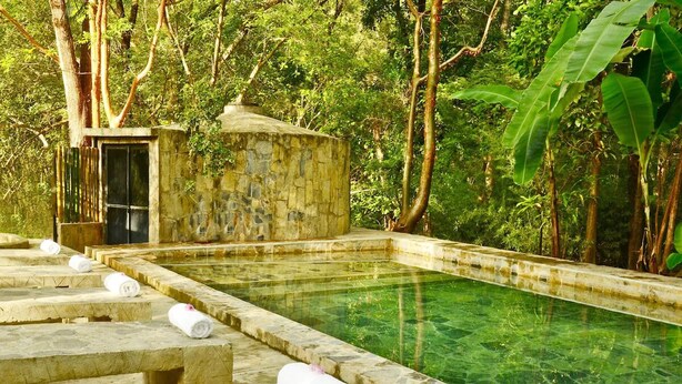 A stone pool with clear water, surrounded by stone steps and a small stone structure. - Hotel Hacienda Concá (Concá)