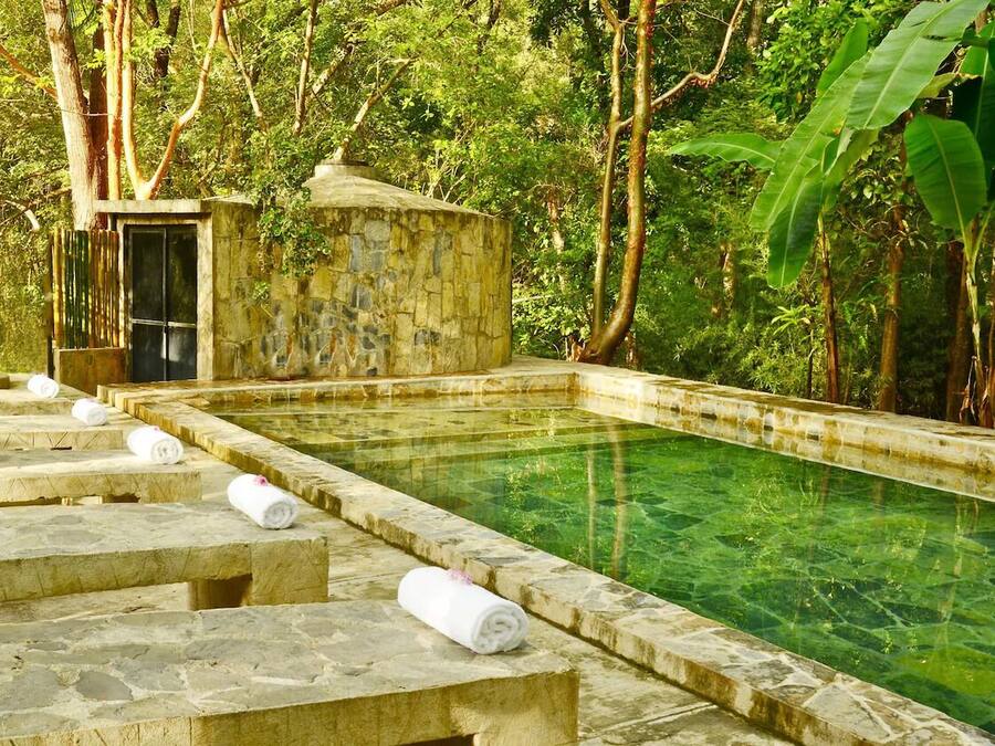 Una piscina de piedra con agua cristalina, rodeada de escalones de piedra y una pequeña construcción de piedra.