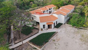 A white building with a red-tiled roof, surrounded by greenery and a paved courtyard. - Hotel Hacienda Concá (Concá)