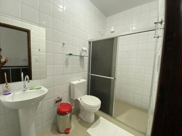 A bathroom with white tiles, a sink, a toilet, and a glass shower enclosure. - APART-HOTEL SALINE LTDA (Salinópolis)