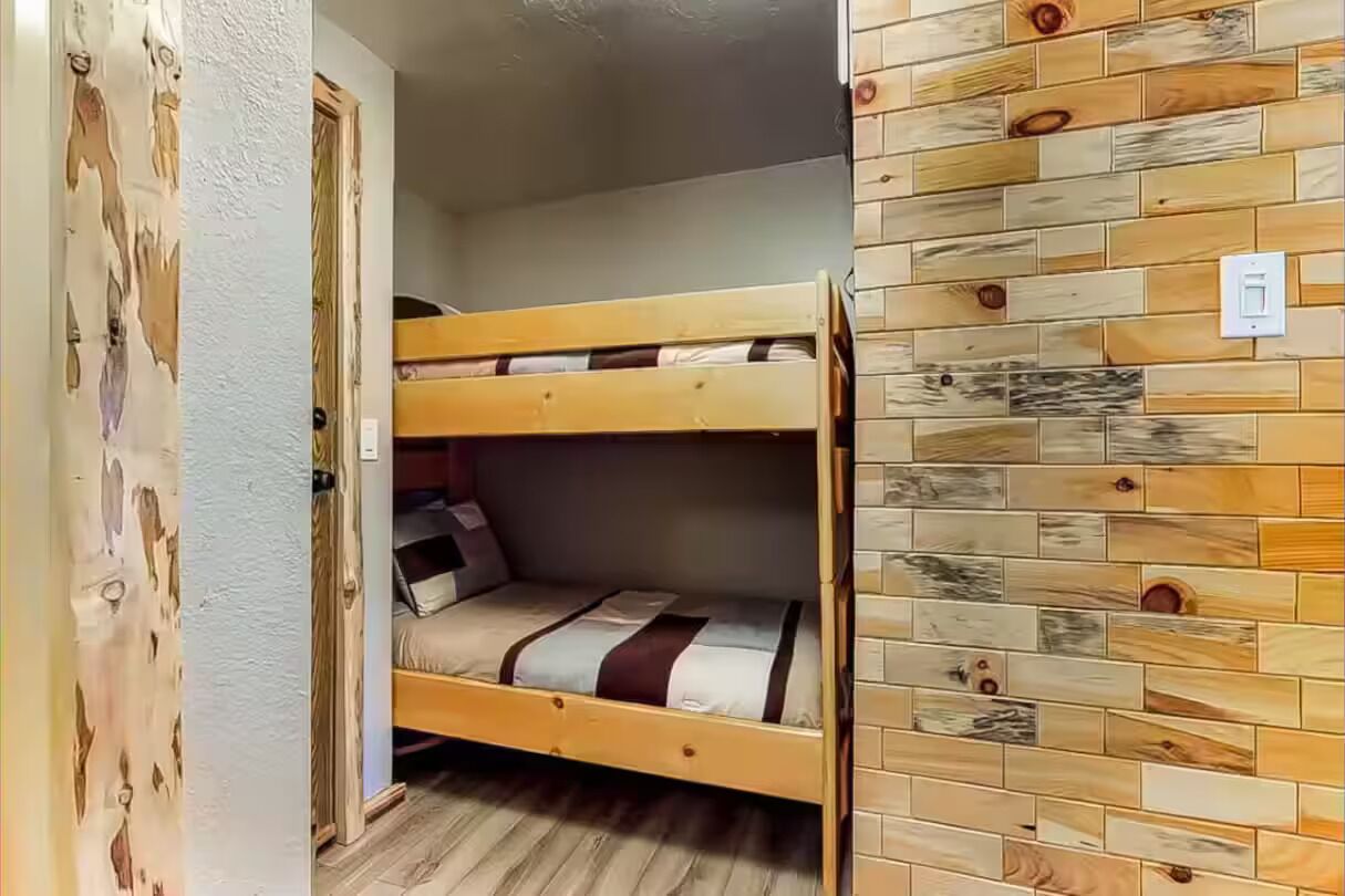 Une chambre avec un lit superposé, un plancher en bois et un mur orné d’un motif imitant le grain du bois.