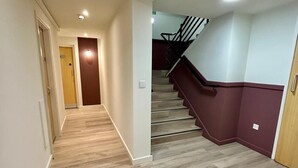 A hallway with wooden flooring, a staircase with red handrails, and a door at the end. - Student Only The Railyard (Liverpool)