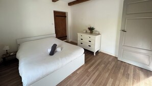 Un dormitorio con cama, mesita de noche, cómoda, puerta de madera y techo con vigas a la vista.