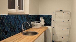 Una cocina con encimera de madera, un fregadero, una ventana, una lavadora y un tendedero.