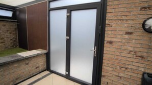 Uma entrada de prédio moderna, com porta de vidro, parede de tijolos e piso ladrilhado.