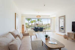 A modern living room with a sofa, coffee table, and TV. There is a balcony with a view of palm trees and buildings. - Snazzy Varandas do Castelo One-bedroom Apartment Sleeps 2 Person (Albufeira)