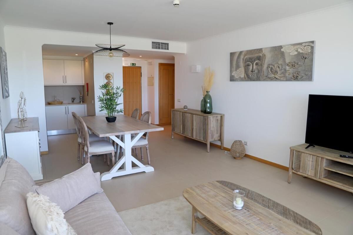 A modern living room with a sofa, a dining table with chairs, a TV stand, and a painting on the wall.