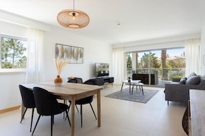 A modern living room with a dining area, large windows, and a balcony. - Snazzy Varandas do Castelo One-bedroom Apartment Sleeps 2 Person (Albufeira)