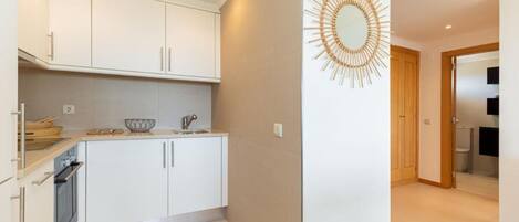 A modern kitchen with white cabinets, a built-in oven, and a countertop with a sink and a decorative mirror.