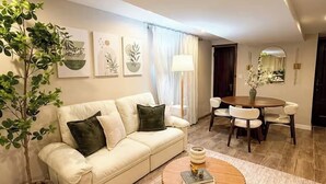 A living room with a sofa, a coffee table, a dining table with chairs, and a potted plant. - Sleeps 26 • Modern Multi-Unit • Gym • Workspaces (Chicago)