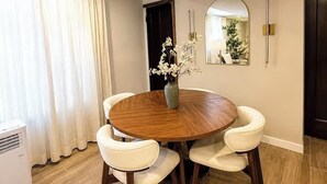 A dining area with a round wooden table, white cushioned chairs, a vase with white flowers, a mirror, and a dark door. - Sleeps 26 • Modern Multi-Unit • Gym • Workspaces (Chicago)