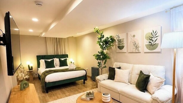 A modern hotel room with a bed, a sofa, a coffee table, a TV, and artwork on the wall. - Sleeps 26 • Modern Multi-Unit • Gym • Workspaces (Chicago)