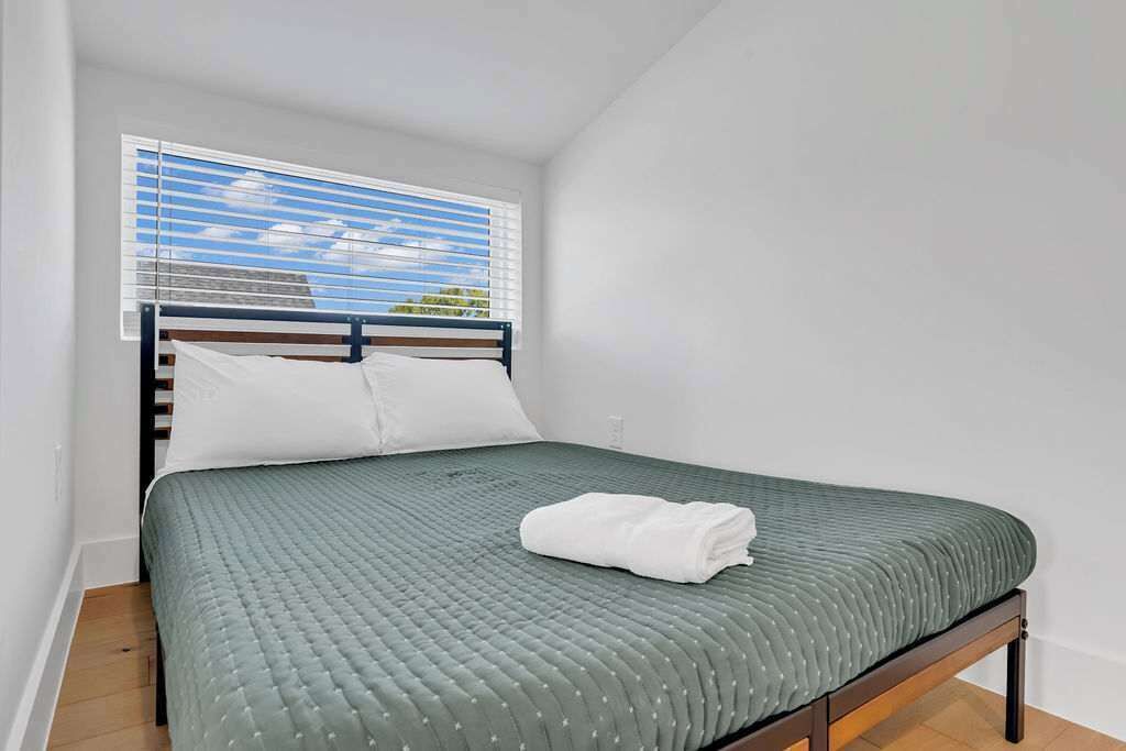 A single bed with a green quilt, white pillows, and a folded white towel.