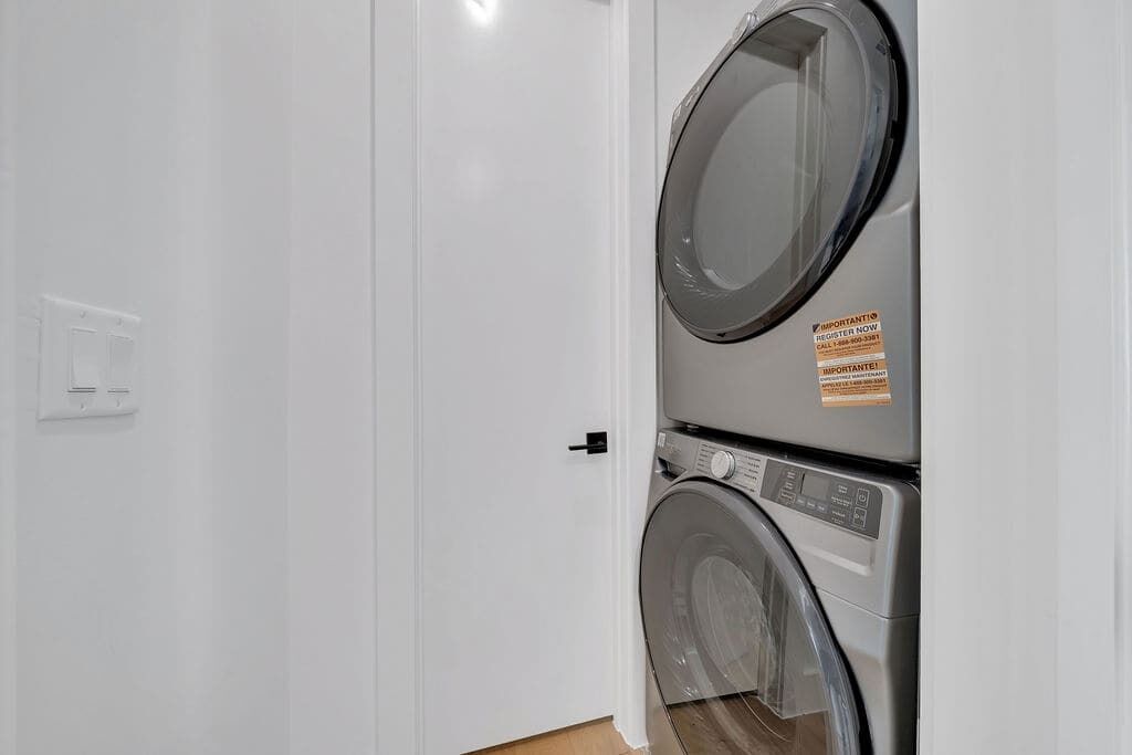 Uma lavanderia com duas máquinas de lavar roupa empilhadas e uma porta branca.