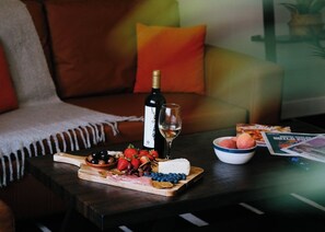 Una tabla de madera con queso, fresas y aceitunas sobre una mesa. También hay una botella de vino y una copa sobre la mesa.