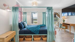 Een slaapkamer met hemelbed, bureau, stoel en televisie.