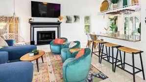 Een woonkamer met een open haard, blauwe banken, een plafondventilator en een bar.