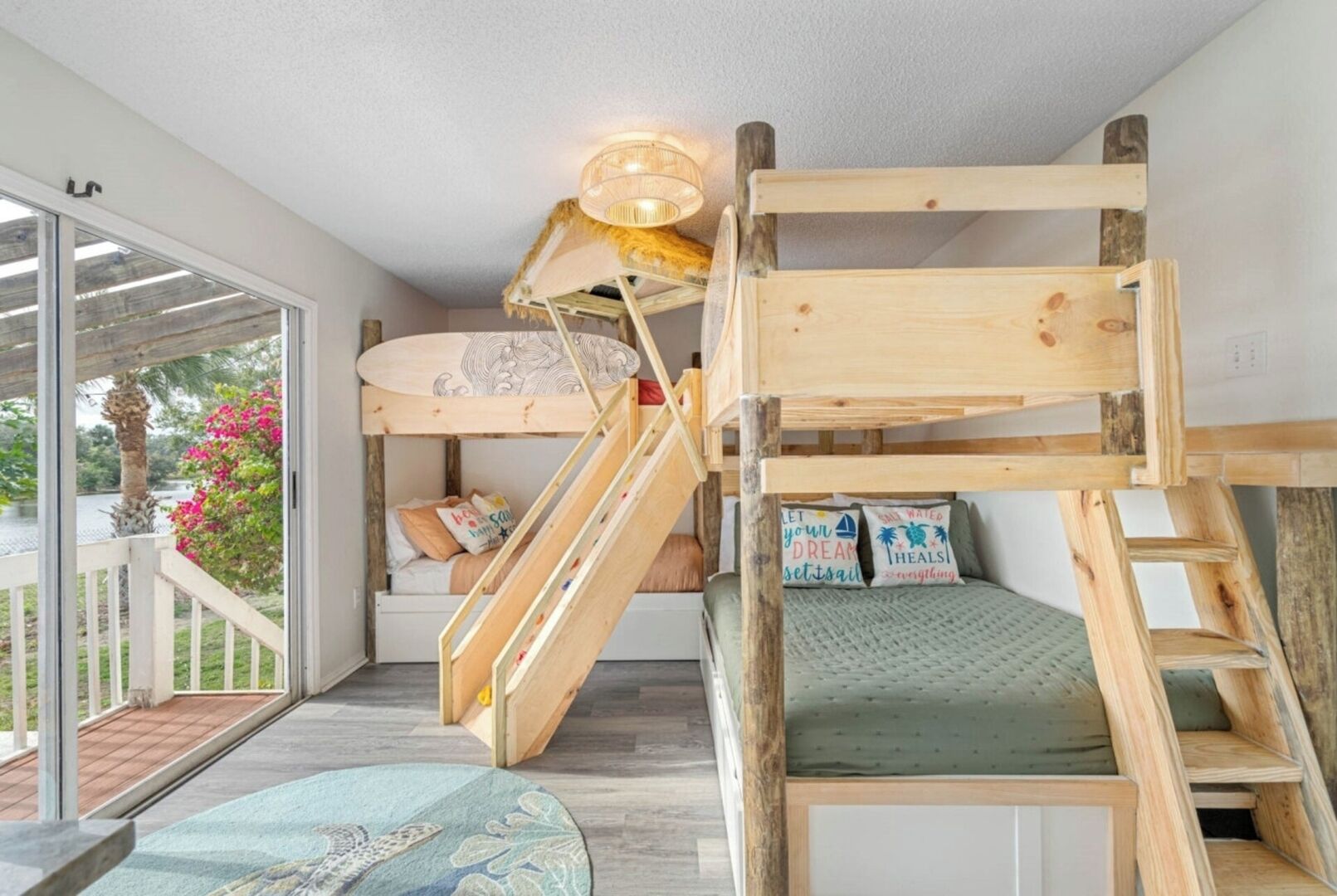 A bunk bed with a slide, a small staircase, and a window with a view of greenery.