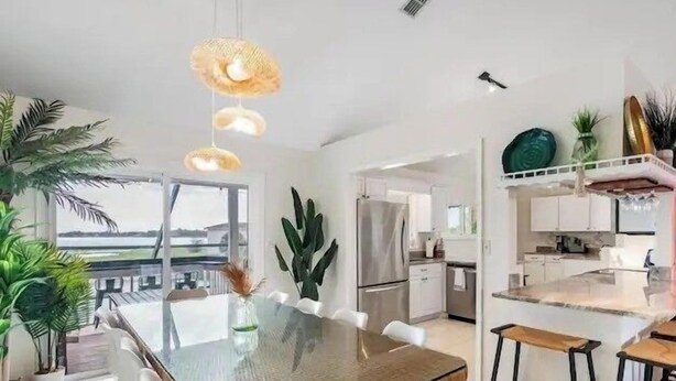 Een moderne keuken met een glazen eettafel, witte stoelen en uitzicht op zee.