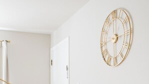 A room with a wooden floor, a white door, a wall-mounted clock, and a small table with a bowl. - 2BR • Newly Furnished Modern Apt • Near O'Hare (Chicago)