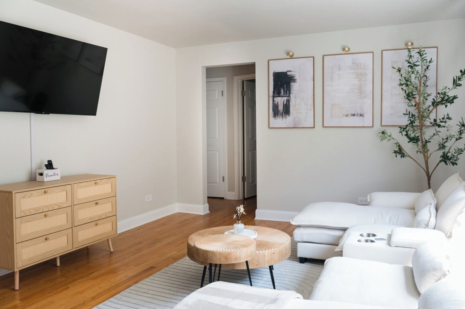 A modern living room with a white sofa, a wooden coffee table, and a TV mounted on the wall.