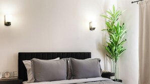 A bedroom with a bed, two bedside tables, a wall clock, a potted plant, and a window with curtains. - 2BR • Newly Furnished Modern Apt • Near O'Hare (Chicago)