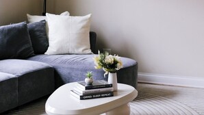 Ein modernes Wohnzimmer mit einem grauen Sofa, einem weißen Couchtisch mit Büchern und einer Vase sowie einer Wanduhr.