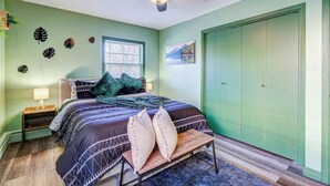 Slaapkamer met een bed, nachtkastje, bankje, plafondventilator, raam en een groene garderobe.