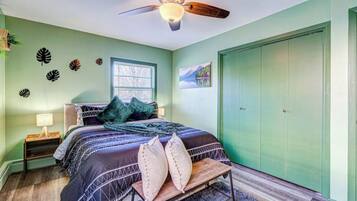 A bedroom with a bed, a nightstand, a bench, a ceiling fan, a window, and a green wardrobe.