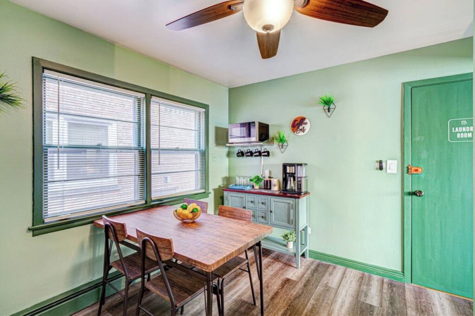 Une cuisine compacte comprenant une table à manger, des chaises, un ventilateur de plafond et une porte verte portant l’inscription « laverie ».