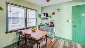 Een kleine keuken met een eettafel, stoelen, een plafondventilator en een groene deur met de tekst