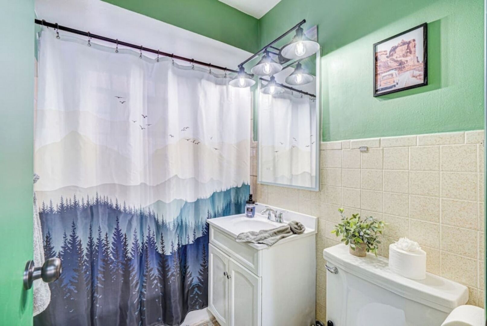 Une salle de bain avec un rideau de douche à motifs de forêt, un lavabo, un miroir et des toilettes.