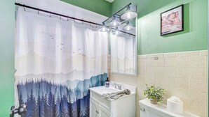 Een badkamer met een douchegordijn met bosmotief, een wastafel, een spiegel en een toilet.
