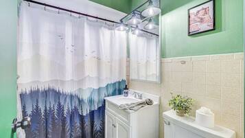 Une salle de bain avec un rideau de douche à motifs de forêt, un lavabo, un miroir et des toilettes.