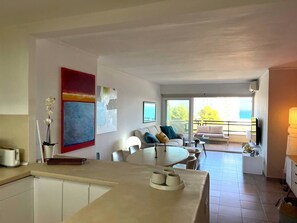 A modern living room with a dining area, a kitchen, and a balcony with a view. - Sea View Apartment Between Forest and Beach – Cala Vinyes (Badia de Palma)
