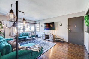 A modern living room with a green sofa, a coffee table, and a TV on the wall. - Top Rated Condo •King Bed • Safe Historic Location (Elmwood Park)