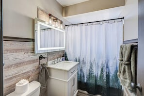 A bathroom with a wooden wall, a white sink, a mirror, and a shower curtain with a forest design. - Top Rated Condo •King Bed • Safe Historic Location (Elmwood Park)