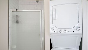 A bathroom with a glass shower enclosure and a white washing machine. - Private Workspace •  Sleeps4 • Modern Stylish Stay (Chicago)