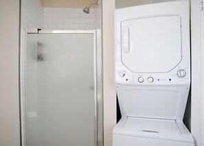 Baño con cabina de ducha de vidrio y lavadora blanca.
