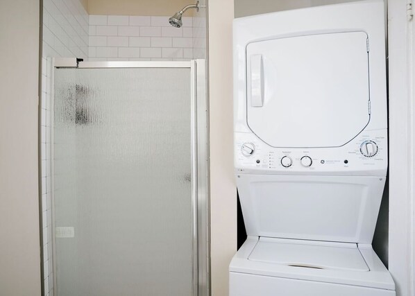 A bathroom with a glass shower enclosure and a white washing machine. - Private Workspace • Sleeps 4 • Modern and Stylish (Chicago)