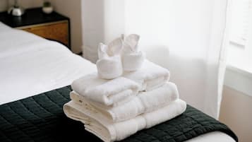 A neatly made bed with a dark green quilt and a stack of white towels on top.
